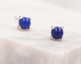 May include: A pair of silver stud earrings with a round blue lapis lazuli gemstone in each earring.