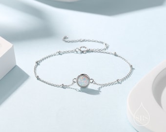Peut inclure: Un bracelet délicat en argent avec un pendentif rond en opale. La chaîne est ornée de petites perles et d'un fermoir à ressort.