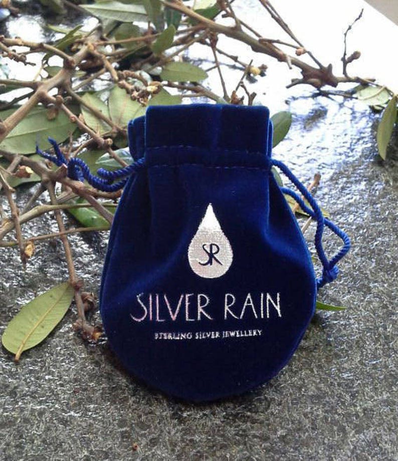 Puede incluir: Una bolsa de terciopelo azul con un logotipo de gota de lluvia plateada y el texto "Silver Rain Sterling Silver Jewellery".