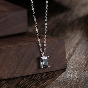 Peut inclure: Un collier en chaîne argent avec un pendentif de forme carrée orné d'une grande pierre précieuse irisée. La pierre précieuse présente un arc-en-ciel de couleurs, notamment le vert, le bleu, le violet et le rouge.