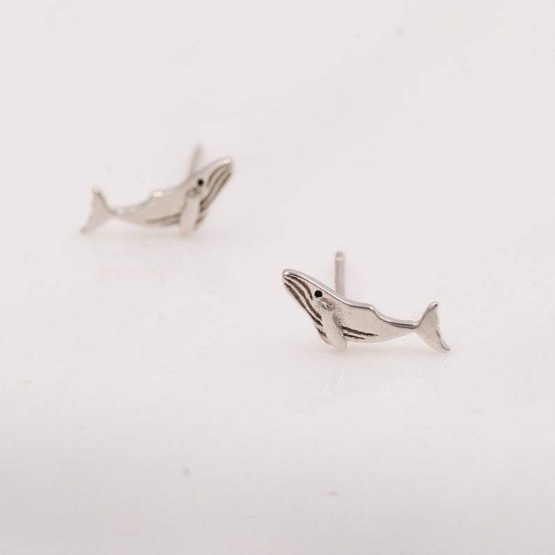 May include: A pair of silver whale stud earrings. The whales are facing upwards with their tails pointing to the right.