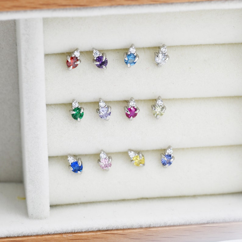 May include: A display case with 12 small, colorful gemstone earrings with a single diamond accent. The earrings are arranged in three rows of four.