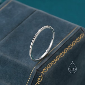 May include: A simple silver band ring with a hammered texture. The ring is on a blue velvet background.