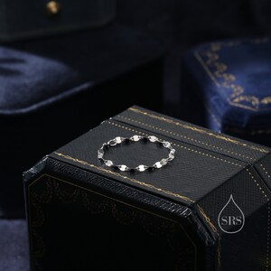 May include: A silver bracelet with a chain made of small, round links. The bracelet is lying on a black box with gold accents and the text "SRS" in a water drop logo.