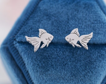 May include: A pair of silver fish-shaped stud earrings on a blue velvet background.