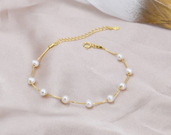 Peut inclure: Un bracelet délicat en chaîne dorée avec de petites perles blanches. Le bracelet est doté d'un fermoir à mousqueton.
