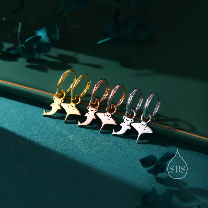 May include: Five hoop earrings with a small hammerhead shark charm hanging from each. The hoops are in different metal finishes: gold, rose gold, and silver.