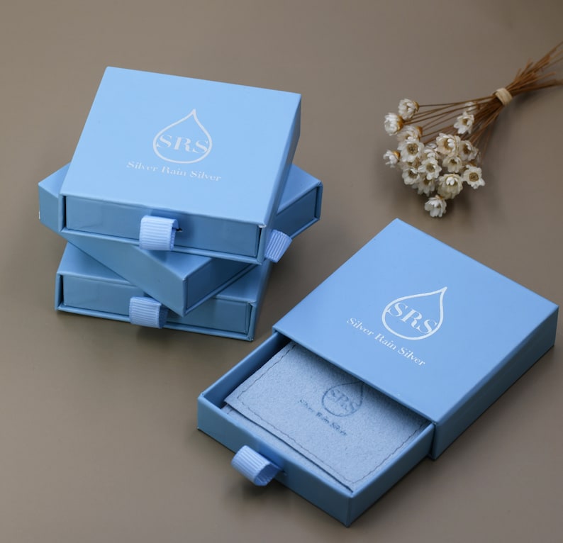 May include: Three light blue boxes with a white raindrop logo and the text "SRS Silver Rain Silver" stacked on top of each other. The top box is open and reveals a blue velvet interior.