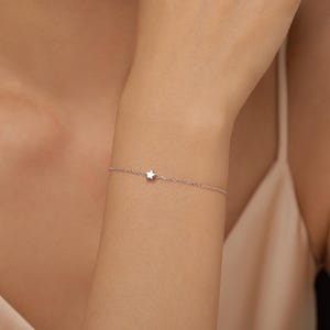 May include: A delicate silver-toned chain bracelet featuring a single, small, five-pointed star charm centred on the wrist. The bracelet is constructed with fine, thin links that create a subtle and understated appearance on the skin.