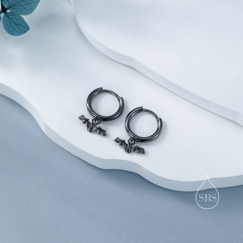May include: A pair of black hoop earrings with a small bat charm hanging from each hoop.