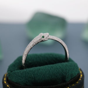 May include: A silver snake ring with a green gemstone eye. The ring is in a green velvet box.