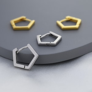 May include: Three hexagonal hoop earrings, two gold and one silver, displayed on a gray surface.