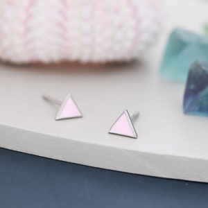 May include: A pair of silver triangle stud earrings with pink enamel. The earrings are small and delicate.