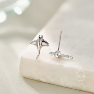 May include: A pair of silver earrings featuring a manta ray design. The earrings are small and delicate, perfect for everyday wear.