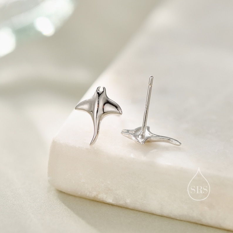 May include: A pair of silver earrings featuring a manta ray design. The earrings are small and delicate, perfect for everyday wear.