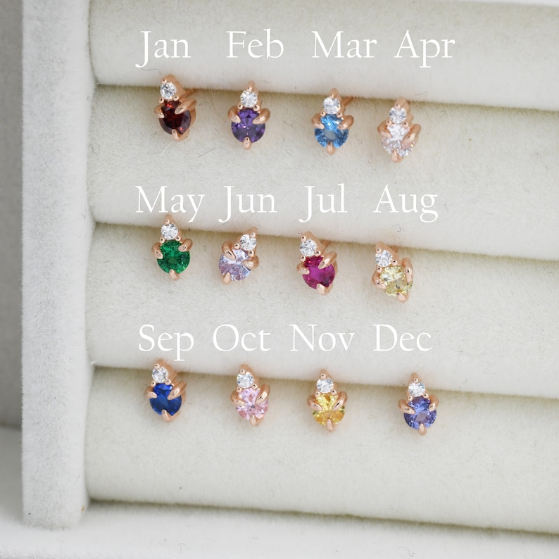 May include: A display of 12 small earrings with different colored gemstones, each with a small diamond accent. The earrings are arranged in a grid with the months of the year labeled above each row.