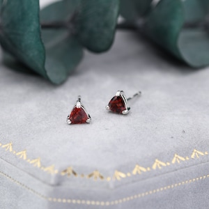 May include: A pair of silver stud earrings with triangular red gemstones.