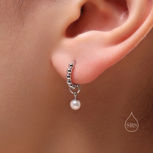 May include: A silver hoop earring with a small pearl dangling from it. The earring is worn in the left ear of a person.
