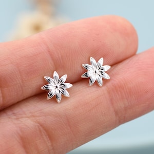 May include: A pair of silver flower stud earrings. The earrings are small and delicate, with a simple design.