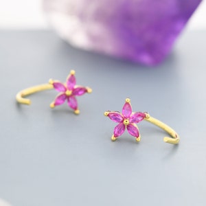 Peut inclure: Une paire de boucles d'oreilles dorées avec des accents en forme de fleurs roses. Chaque boucle d'oreille présente une petite fleur à cinq branches avec des pierres de zircone cubique roses.