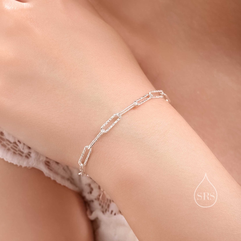 May include: A silver chain bracelet with a textured, oval link design.