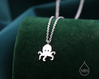 Puede incluir: Collar de plata con un pequeño colgante de pulpo. El collar está sobre un fondo de terciopelo verde.