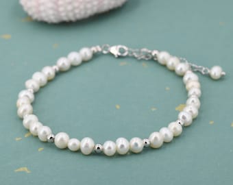 Peut inclure: Un bracelet composé d'une rangée de petites perles d'eau douce blanches de forme irrégulière, alternées avec de minuscules perles métalliques argentées polies. Le bijou est doté d'un fermoir mousqueton argenté et d'une chaînette d'extension.
