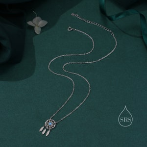May include: A silver-toned necklace featuring a circular dreamcatcher pendant with a small, round, light blue stone at its center. Three delicate silver-toned feather charms hang from the bottom of the pendant. The chain includes a lobster clasp.