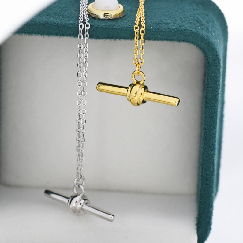 May include: Two necklaces with a toggle clasp pendant. One necklace has a silver chain and a silver pendant. The other necklace has a gold chain and a gold pendant.