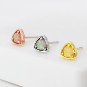 May include: Three triangle-shaped earrings with opal stones set in a silver, gold, and rose gold setting.