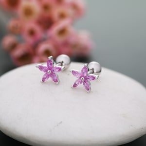May include: A pair of silver flower stud earrings with pink gemstones. The earrings are designed with a small ball post and a flower-shaped charm.
