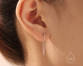 May include: A close-up of a person's ear with a silver chain earring hanging down. The earring is a simple chain with no other embellishments.