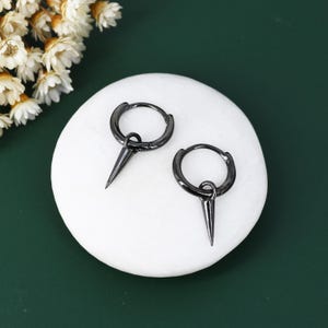 May include: A pair of black hoop earrings with a sharp, pointed spike hanging from each hoop.