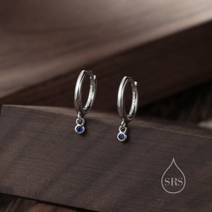 May include: A pair of silver hoop earrings with a small blue gemstone dangling from each hoop.