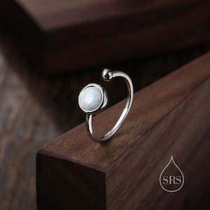 Op de afbeelding: Een zilveren ring met een witte opaal-steen gezet in een ronde bezel. De ring heeft een eenvoudig, modern ontwerp en is perfect voor dagelijks gebruik.