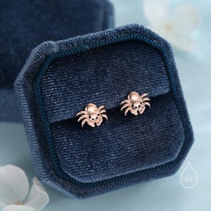 May include: A pair of rose gold spider earrings in a blue velvet jewelry box.