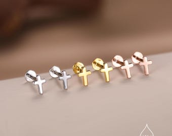 May include: A collection of cross-shaped stud earrings in silver, gold, and rose gold tones. The earrings are displayed on a neutral surface, showcasing their different metallic finishes. The crosses have a simple, elegant design.