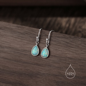 May include: A pair of silver teardrop earrings with light blue opal stones.