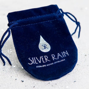 Puede incluir: Una bolsa de terciopelo azul oscuro con cord&oacute;n que presenta un logotipo met&aacute;lico plateado de una gota de lluvia con las letras SR en su interior. Debajo del logotipo, el texto dice SILVER RAIN y STERLING SILVER JEWELLERY en una fuente plateada sin remates.