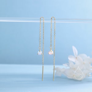 May include: A pair of gold chain earrings with a small opal gemstone at the end of each chain. The earrings are hanging from a clear rod.