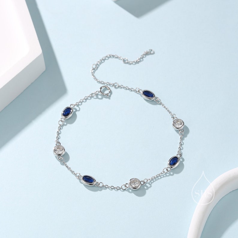 Peut inclure: Un bracelet en argent avec une cha&icirc;ne et des pierres ovales bleues et transparentes altern&eacute;es.