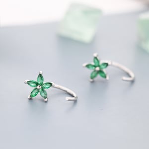 May include: A pair of silver earrings with a green flower design. Each earring features a five-pointed star with green gemstones.