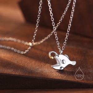 May include: Silver chain necklace with a silver anglerfish pendant. The anglerfish has a gold lure.