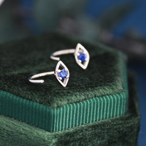 May include: A pair of silver earrings with a diamond-shaped design and a blue gemstone in the center.