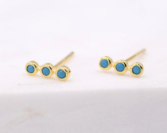 May include: A pair of gold stud earrings with three turquoise blue stones in a row.