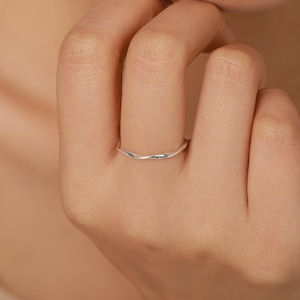 May include: A thin, polished silver ring featuring a subtle, continuous wavy or twisted design that encircles the finger. The band has a smooth, reflective metallic surface with a delicate, undulating shape that creates a soft, flowing appearance.