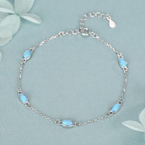 Peut inclure: Un bracelet en argent délicat orné d'opales ovales bleu clair. La chaîne fine est ponctuée d'opales espacées régulièrement. Le fermoir est réglable. Le bracelet mesure environ 18 cm de long.