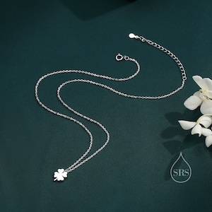 May include: A silver necklace with a four-leaf clover pendant. The necklace is on a green background.