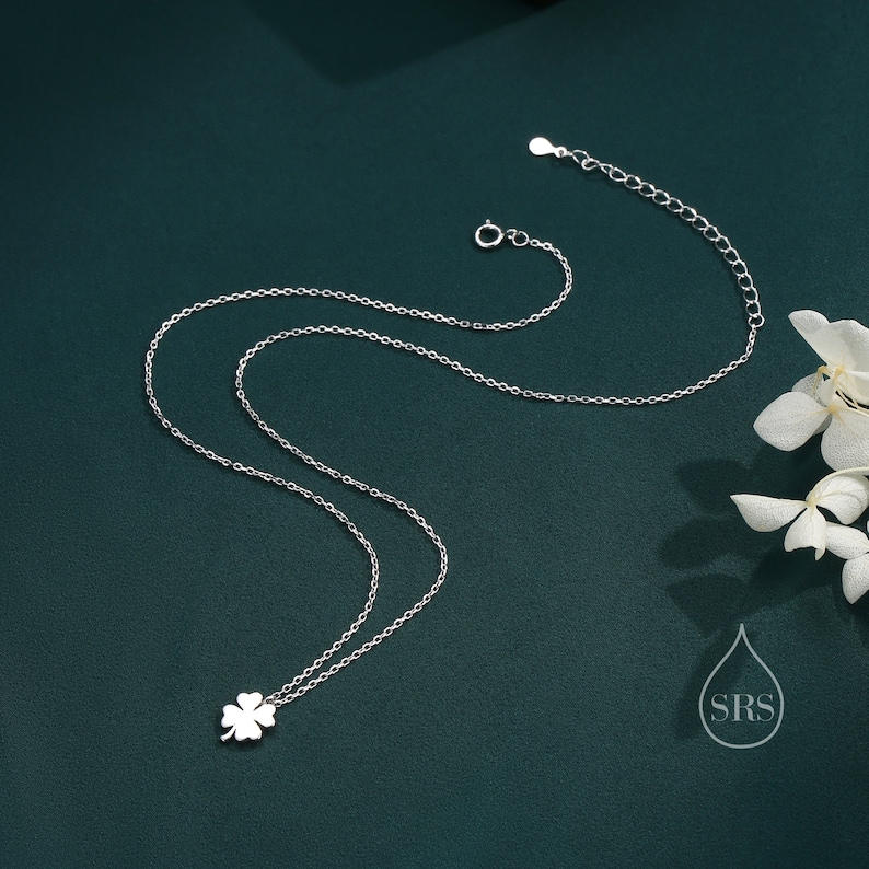 May include: A silver necklace with a four-leaf clover pendant. The necklace is on a green background.