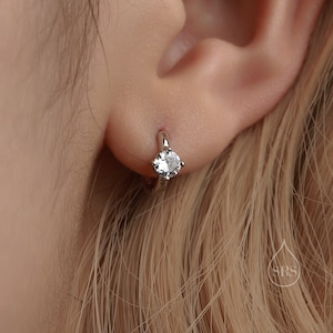 May include: A silver hoop earring with a clear round gemstone in the centre.